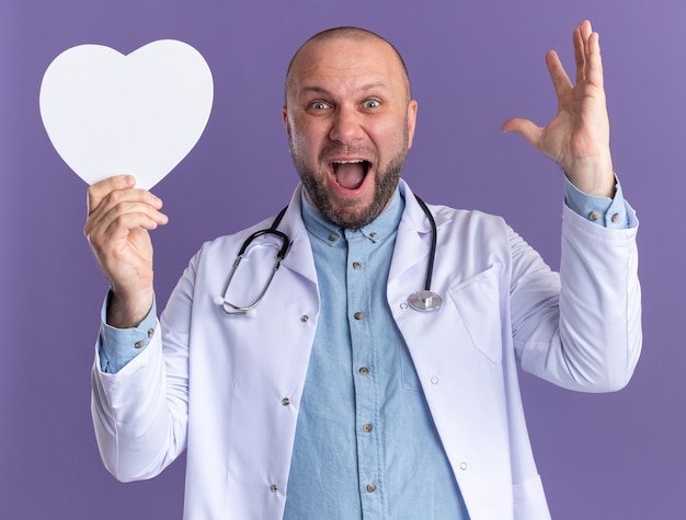 Onder de indruk mannelijke arts van middelbare leeftijd die een medisch gewaad en een stethoscoop draagt met een hartvorm die de hand opsteekt