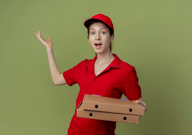 Onder de indruk van een jong, mooi bezorgmeisje in een rood uniform en een pet die pizzapakketten vasthoudt en lege hand toont showing