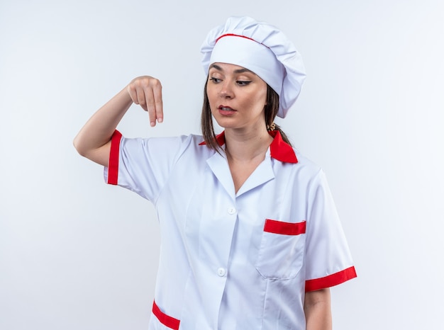 Onder de indruk van een jonge vrouwelijke kok die een uniform van een chef-kok draagt en doet alsof hij iets vasthoudt dat op een witte muur is geïsoleerd
