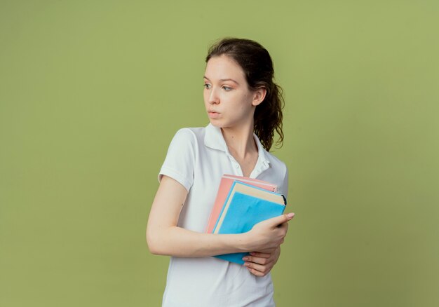 Onder de indruk van het jonge mooie vrouwelijke boek en het notitieblok van de studentenholding die kant bekijken die op olijfgroene achtergrond met exemplaarruimte wordt geïsoleerd