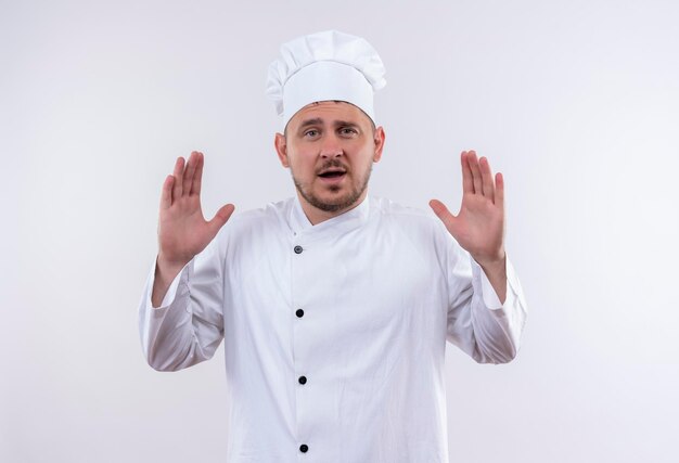 Onder de indruk van jonge knappe kok in uniform van de chef-kok met lege handen geïsoleerd op een witte muur