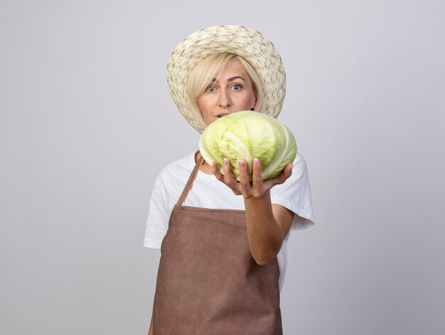 Onder de indruk van middelbare leeftijd blonde tuinman vrouw in uniform met hoed die kool uitrekt