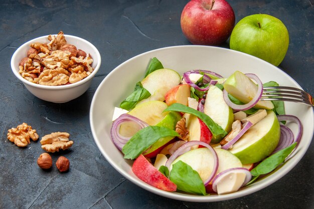 Onderaanzicht appelsalade in kom appelschijfje op vork walnoot in kom rode en groene appels op donkere tafel