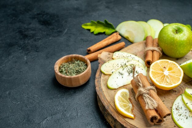 Onderaanzicht appelschijfjes appel gebonden kaneelstokjes en citroenschijfjes op een houten bord met gedroogd muntpoeder op zwarte grond kopieerplaats