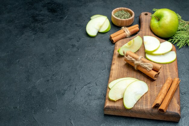 Onderaanzicht appelschijfjes en kaneelstokjes op houten serveerplank gedroogd muntpoeder in kleine kom op donkere tafel met kopieerplaats