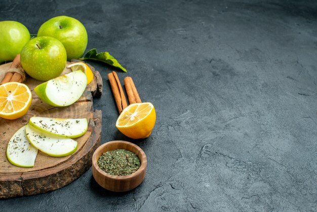 Onderaanzicht appelschijfjes kaneel en citroenschijfjes appel op houten bord gesneden citroen kaneel gedroogde munt in kleine kom op zwarte tafel met kopieerruimte