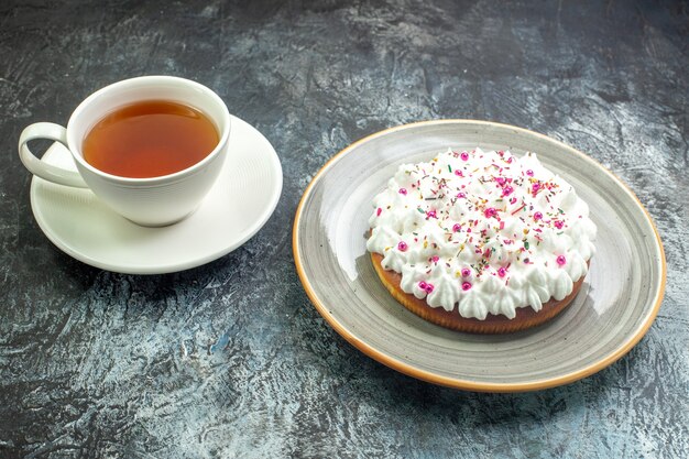 Onderaanzicht cake met witte banketbakkersroom op grijze ronde schotel kopje thee op grijze tafel