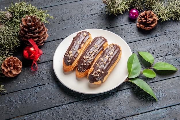 Onderaanzicht chocolade eclairs op een ovale plaat dennenappels kerst speelgoed dennenboom bladeren op donkere houten grond