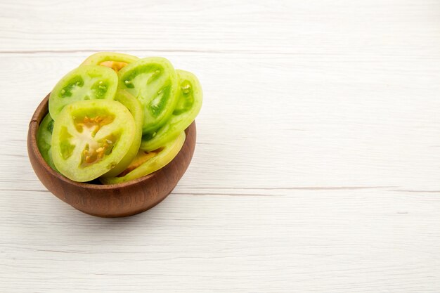 Onderaanzicht gehakte groene tomaten in houten kom op witte tafel met vrije ruimte