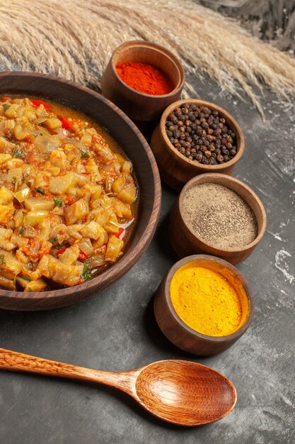 Onderaanzicht geroosterde auberginesalade in kom verschillende kruiden in kleine kommen houten lepel op donkere tafel