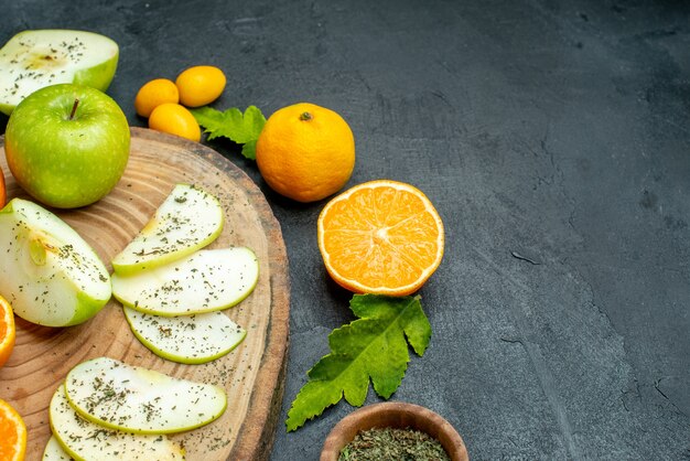 Onderaanzicht gesneden appels en mandarijnen op ronde houten plank cumcuat gedroogd muntpoeder in houten kom op donkere tafel met vrije plaats