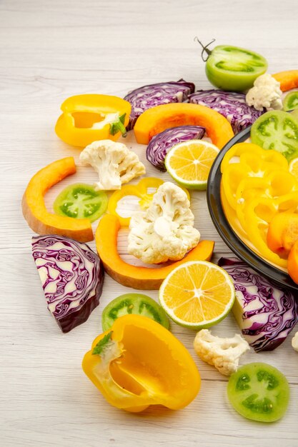 Onderaanzicht gesneden groenten en fruit pompoen gele paprika kaki rode kool groene tomaten op zwarte plaat op houten tafel