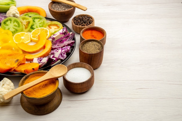 Onderaanzicht gesneden groenten en fruit pompoen paprika persimmon rode kool op zwarte plaat kruiden in kleine kommen houten lepel op houten tafel kopie ruimte