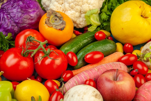 Gratis foto onderaanzicht groenten en fruit radijs kerstomaatjes persimmon tomaten kiwi komkommer appels rode kool peterselie kweepeer op blauwe tafel