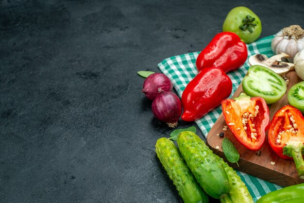 Onderaanzicht groenten tomaten paprika op snijplank knoflook komkommers rode ui op zwarte tafel met kopieerplaats