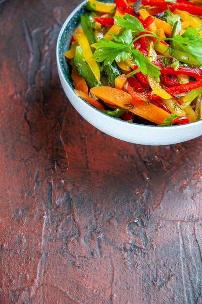 Onderaanzicht groentesalade in kom op donkerrode tafel met vrije plaats