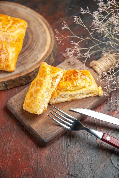 Onderaanzicht penovani khachapuri op houten bord en op snijplank mes en vork op donkerrode tafel