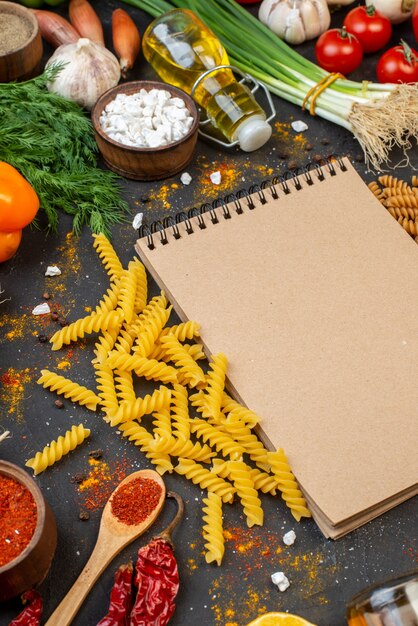 Onderaanzicht rauwe spiraal pasta notebook kurkuma in kleine kom verse groenten olie fles op tafel