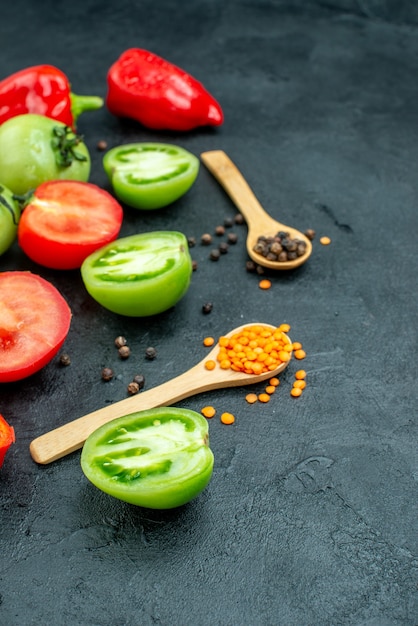 Onderaanzicht rode en groene tomaten gesneden paprika zwarte peper gezellige rode linzen in houten lepels op donkere tafel