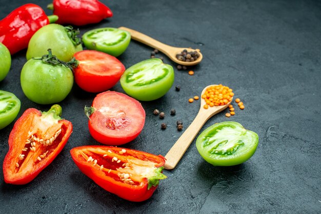 Onderaanzicht rode en groene tomaten gesneden paprika zwarte peper gezellige rode linzen in houten lepels op donkere tafel