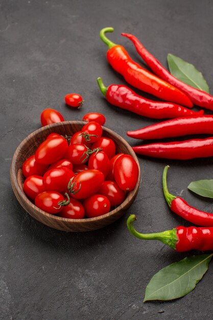 Onderaanzicht rode paprika's en loonblaadjes en een kom met kerstomaatjes op zwarte tafel