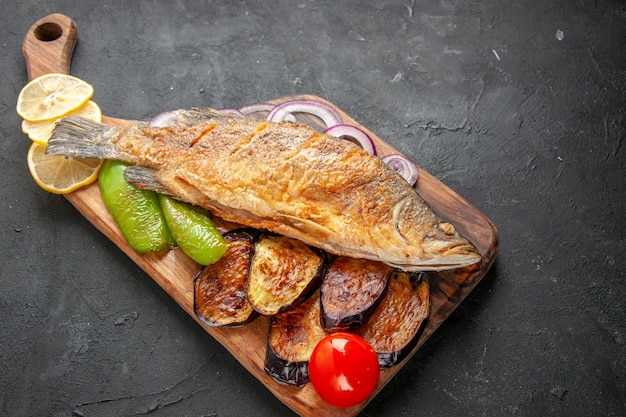 Onderaanzicht smakelijke vis bakken gebakken aubergines ui op houten serveerplank op donkere achtergrond