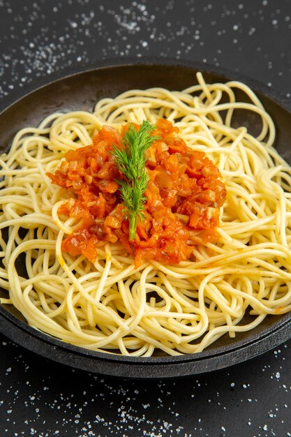 Onderaanzicht spaghetti met saus in koekenpan op zwarte tafel