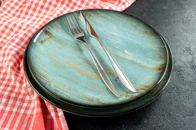 Onderaanzicht stalen vork en diner mes op ronde schotel rood en wit geruit tafelkleed op zwarte tafel