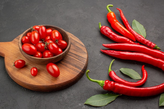 Onderaanzicht van de close-up rode paprika's en loonblaadjes en een kom met kerstomaatjes op het ovale snijbord op zwarte tafel