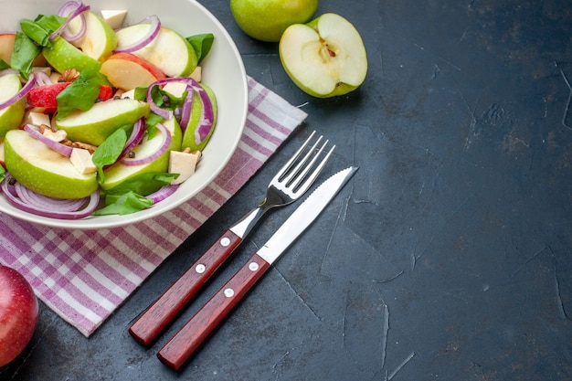 Onderaanzicht verse appelsalade in witte kom appels paars en wit geruit tafelkleed vork en mes op donkere tafel vrije ruimte