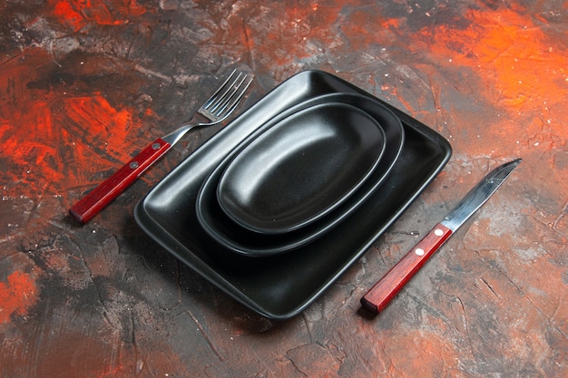 Gratis foto onderaanzicht zwarte ovale en rechthoekige schotels vork en mes op donkerrode tafel