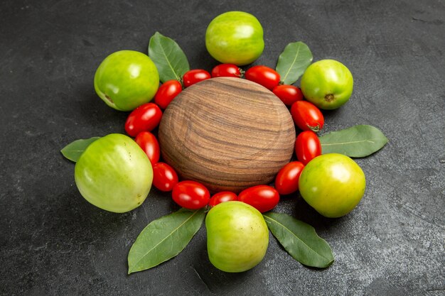 Onderkant sluiten cherry tomaten groene tomaten en laurierblaadjes rond een houten plaat op donkere achtergrond