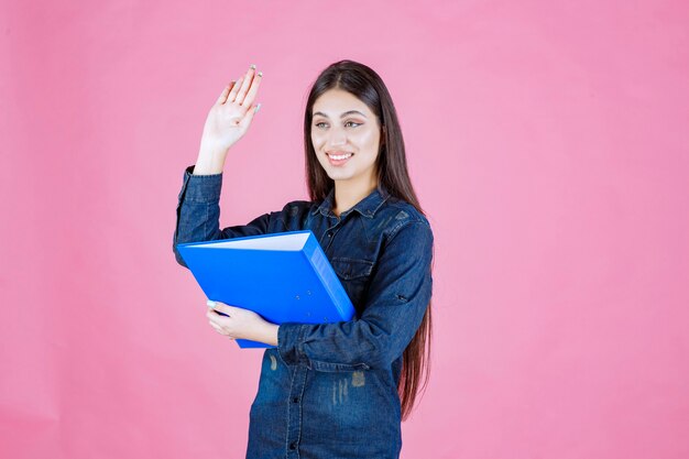 Onderneemster die een blauwe omslag houdt en iemand begroet door hand te schudden