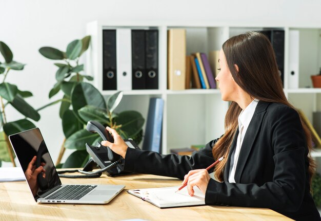 Onderneemster die in agenda met potlood schrijven die de telefoonontvanger nemen