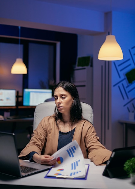 Ondernemer die documenten doorzoekt om 's avonds een deadline af te werken. Zakenvrouw die overwerkt op kantoor om een zakelijke baan af te maken met behulp van tablet-pc.