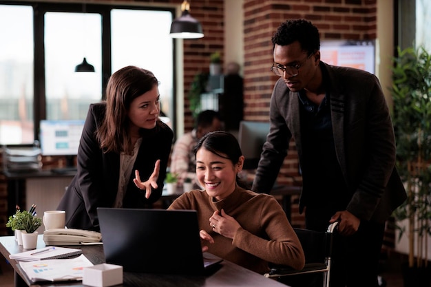 Ondernemers doen startup-teamwerk in een handicapvriendelijk kantoor, met behulp van een laptop om op internet te surfen. Vrouwelijke werknemer rolstoelgebruiker met een beperking die aan projectstrategie werkt.