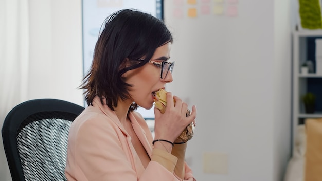 Ondernemersvrouw die smakelijke sandwich eet die werkonderbreking heeft die in zakelijk bedrijf werkt