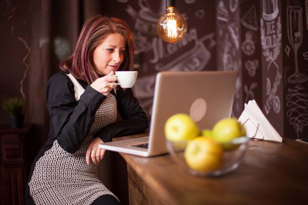 Ondernemersvrouw die van haar koffie voor haar laptop geniet. Ontspannen in een vintage coffeeshop