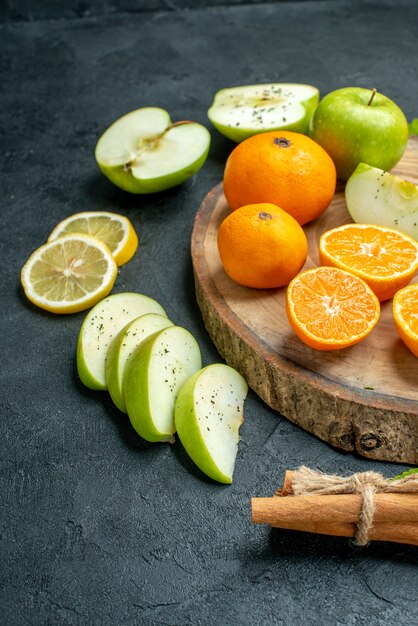 Onderste halve weergave gesneden appels en mandarijnen op ronde houten plank kaneel vastgebonden met touw citroenschijfjes op donkere tafel