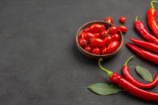 Onderste helft bekijk rode paprika's en loonblaadjes en een kom met kerstomaatjes aan de rechterkant van de zwarte achtergrond