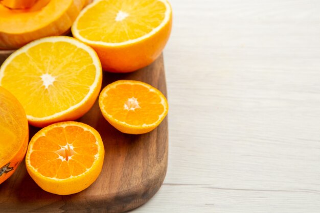 Onderste helft weergave butternut squash in kommen gesneden kaki, mandarijnen en sinaasappels op snijplank op witte tafel vrije ruimte