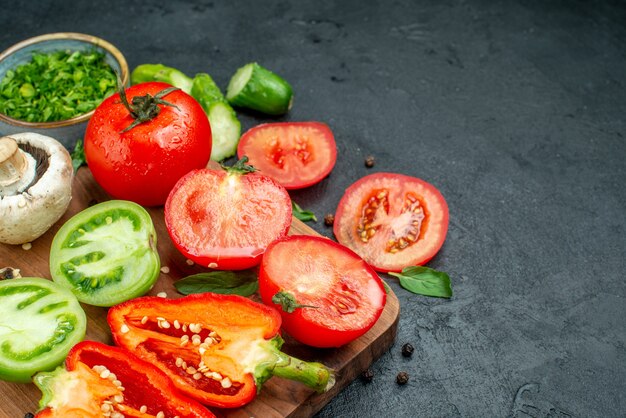 Onderste helft weergave groenten groene en rode tomaten paprika mes op snijplank greens in kom op zwarte tafel vrije ruimte