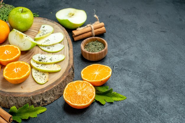 Onderste helft weergave verse appel en sinaasappelschijfjes op houten bord gedroogd muntpoeder in kom kaneelstokjes pijnboomtakken op zwarte tafel vrije ruimte