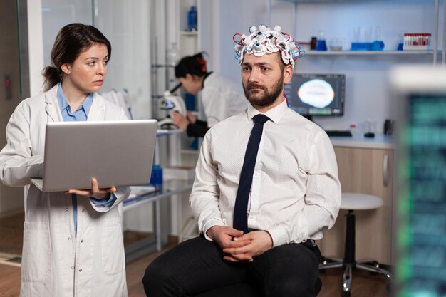 Onderzoeker vrouw arts typen neurologische ziektesymptomen op laptop medische behandeling bespreken met patiënt. Neuroloog-ingenieur die de activiteit van het zenuwstelsel van de mens bewaakt met een eeg-headset