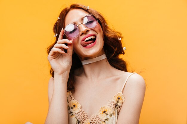 Ondeugende vrouw in lila zonnebril likt haar lippen en poseren op een oranje achtergrond.