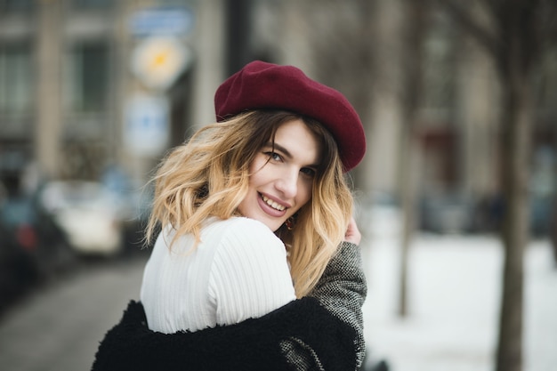 Ondiepe focus shot van een aantrekkelijke gelukkig blonde vrouw in warme winterkleren poseren op straat