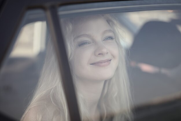 Ondiepe focus shot van een jonge blonde glimlachende vrouw achter het autoraam