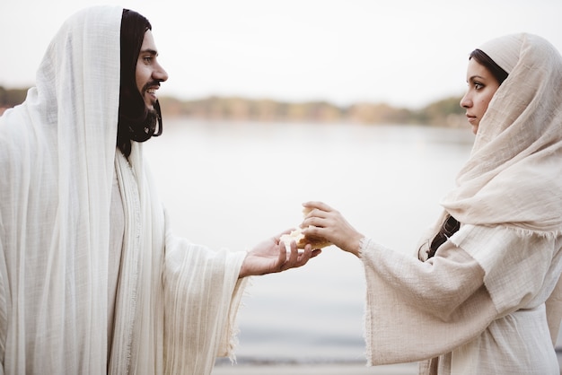 Gratis foto ondiepe focus shot van een vrouw die een bijbelse mantel draagt en het brood uit de hand van jezus christus grijpt