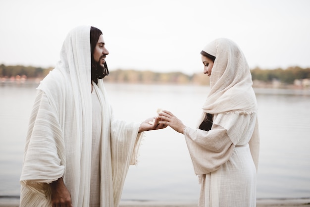 Ondiepe focus shot van Jezus Christus die een stuk brood geeft aan een vrouw die een bijbelse mantel draagt