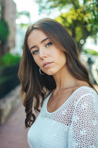 Ondiepe focus van een brunette vrouw die een wit kanten overhemd draagt in een park